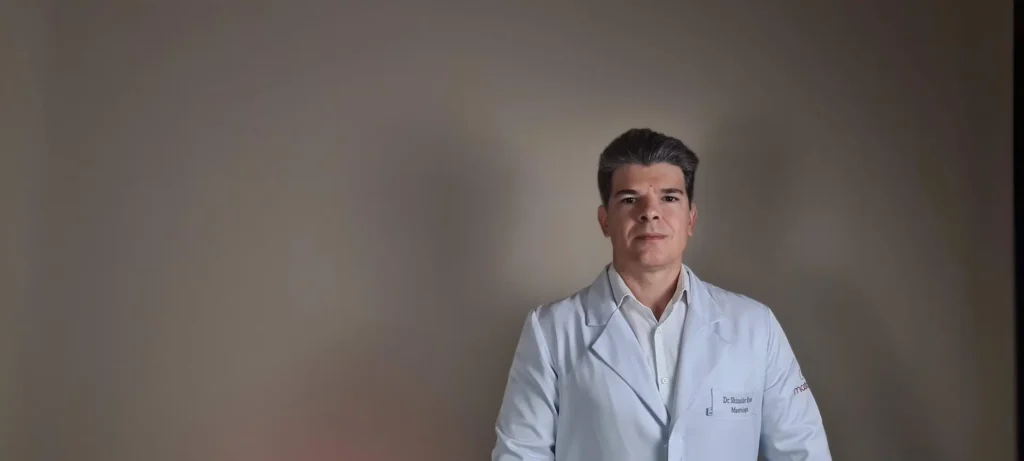 Dr. Shinaider, usando um jaleco branco, olhando para a câmera.
